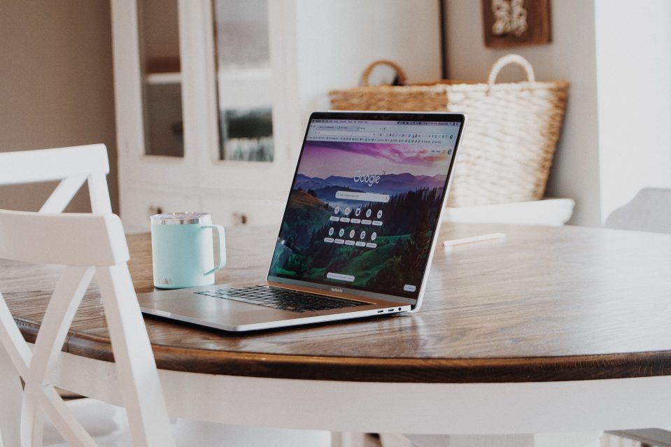 An open laptop with Google on screen on a wooden table with a coffee in the background