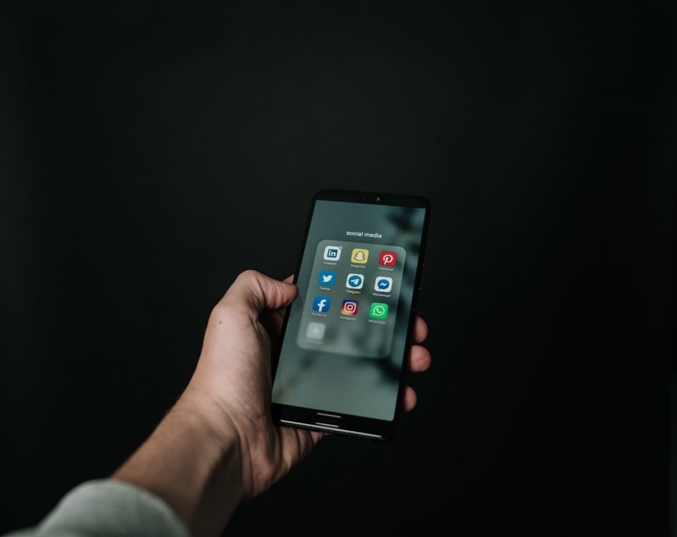 A hand holding an unlocked phone, displaying all the social media icons